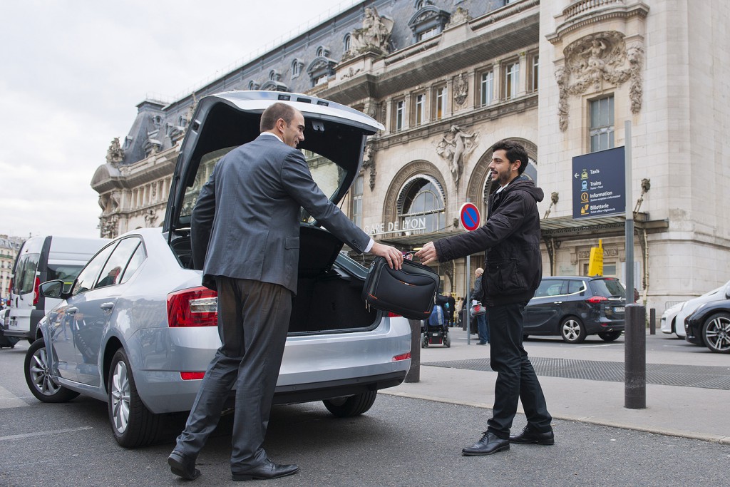 deux hommes un donnant une sacoche à l'autre pour le mettre dans le coffre de la voiture - un taxi devant une gare